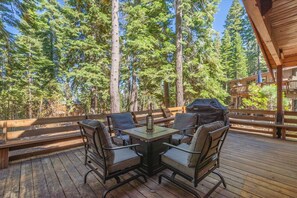 An outdoor deck with a table and chairs, surrounded by tall trees. - Tahoma Family Cabin 3 Bedroom Home (Homewood)