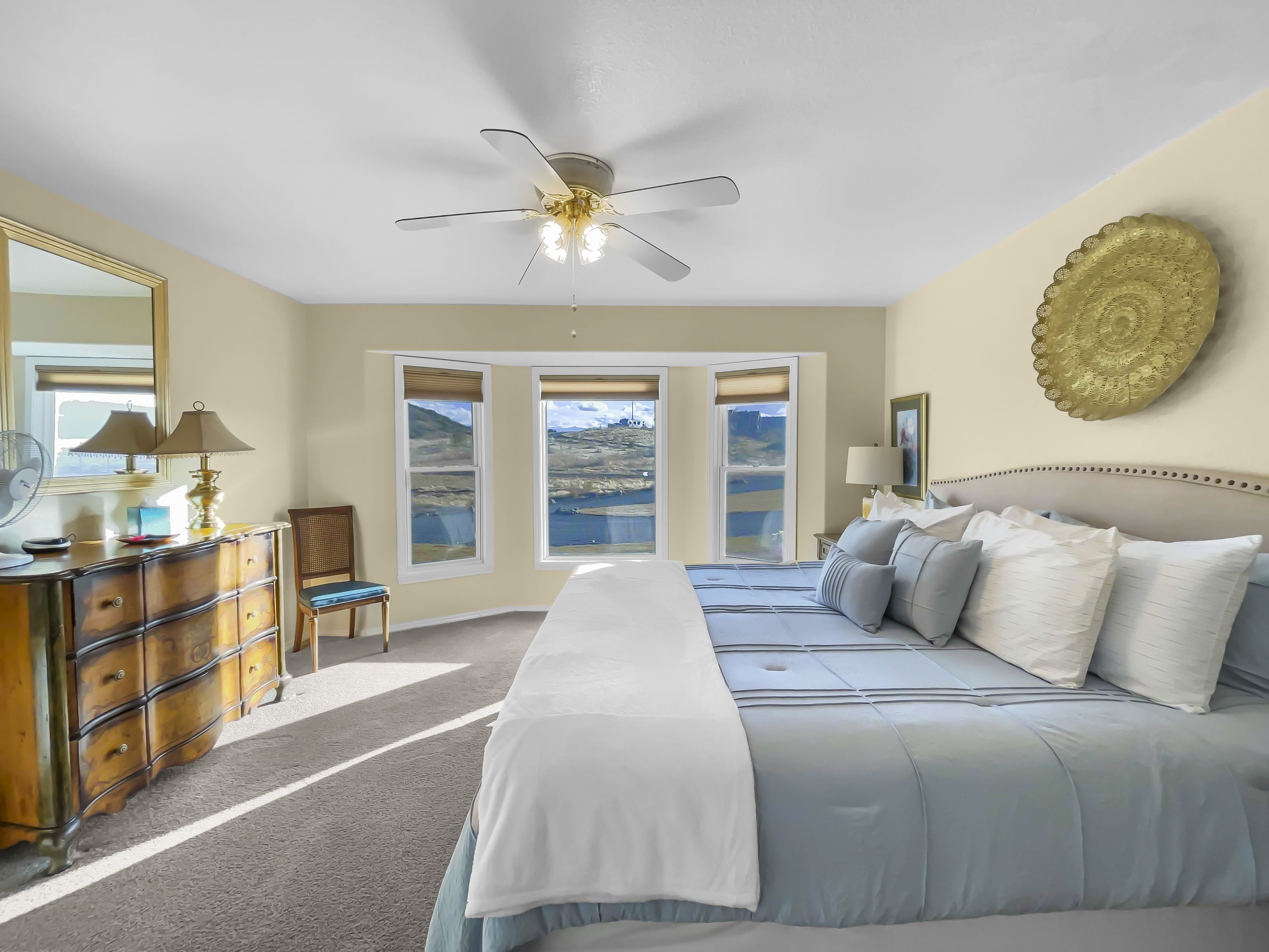 A bedroom with a bed, dresser, chair, and a ceiling fan.
