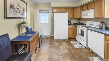 A compact kitchen with a refrigerator, microwave, stove, and oven. There is a dining table with chairs and a ceiling fan.