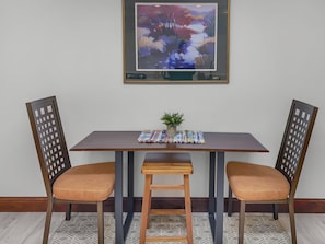 Uma área de refeições com uma mesa de madeira, duas cadeiras e um quadro na parede.