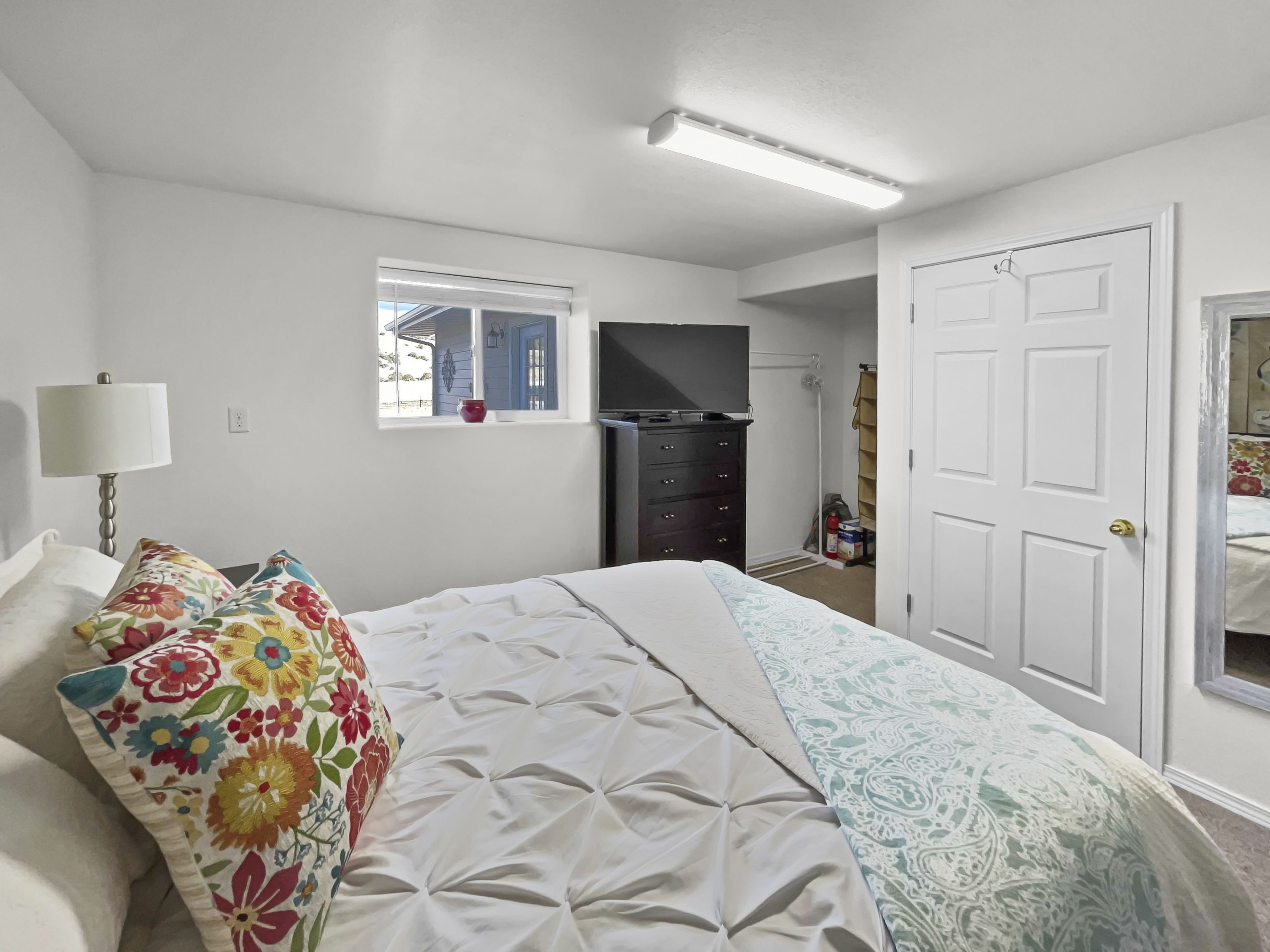 A bedroom with a bed, a dresser, a television, and a window.
