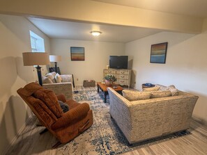 A living room with a sofa, armchair, television, and decorative items. - Forever Family Farm 3 Bedroom Home (Montrose)