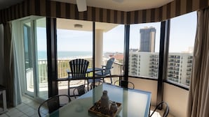 Ein Zimmer mit einem Glastisch, Stühlen und Blick auf das Meer und Gebäude.