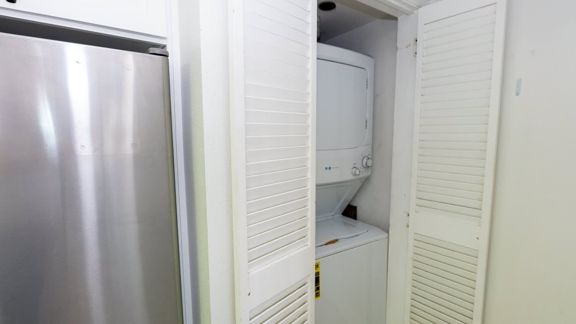 A compact kitchen with a stainless steel refrigerator, a built-in oven, and a white cabinet.