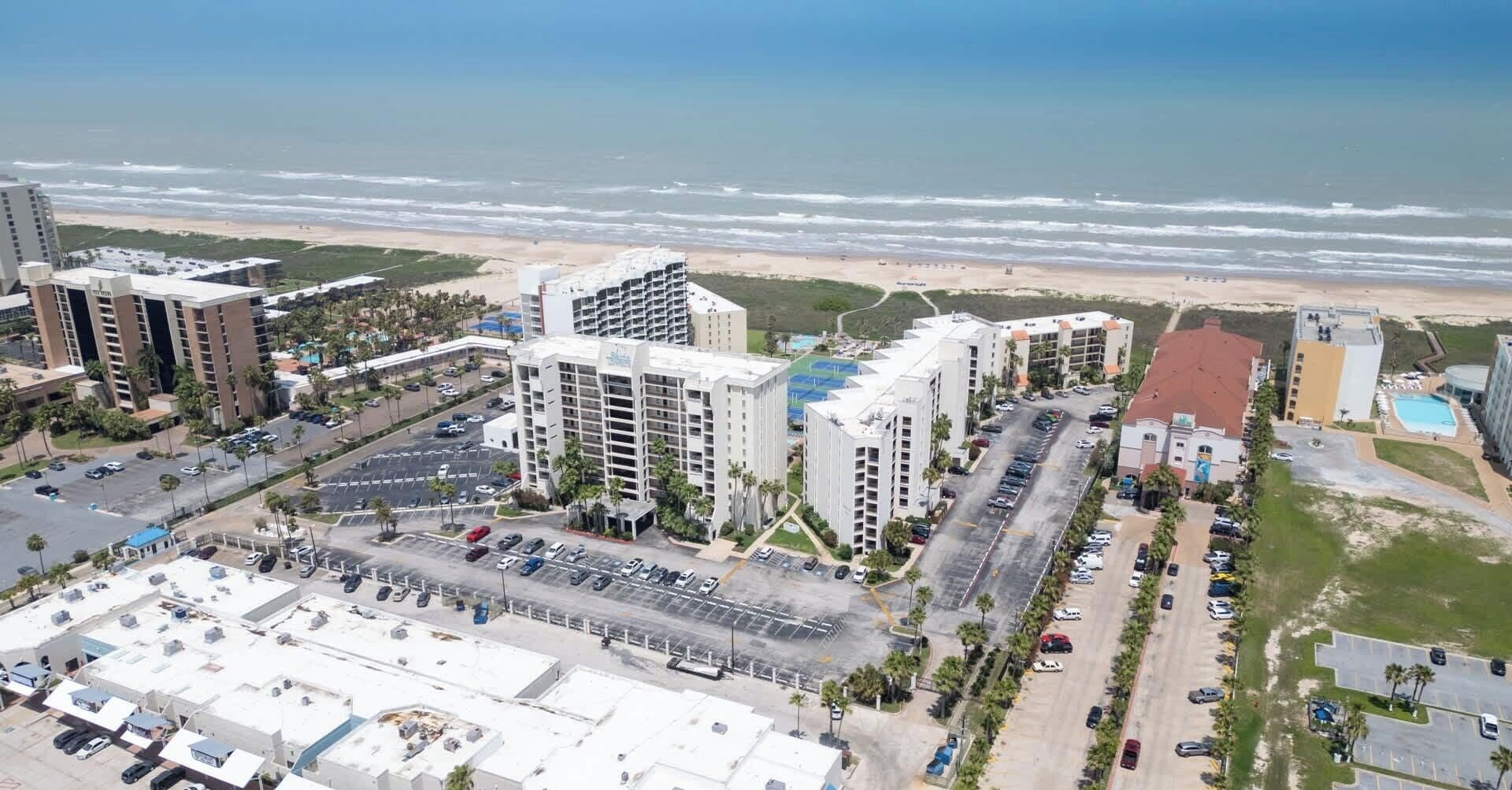 A coastal urban area with high-rise buildings, a beach, and a parking lot.