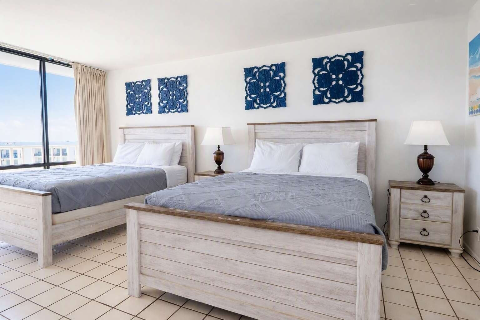 A hotel room with two beds, a large window, and decorative wall art.