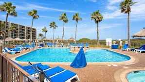 Ein Swimmingpool mit blauen Liegestühlen und Palmen, umgeben von einem Hotelgebäude.