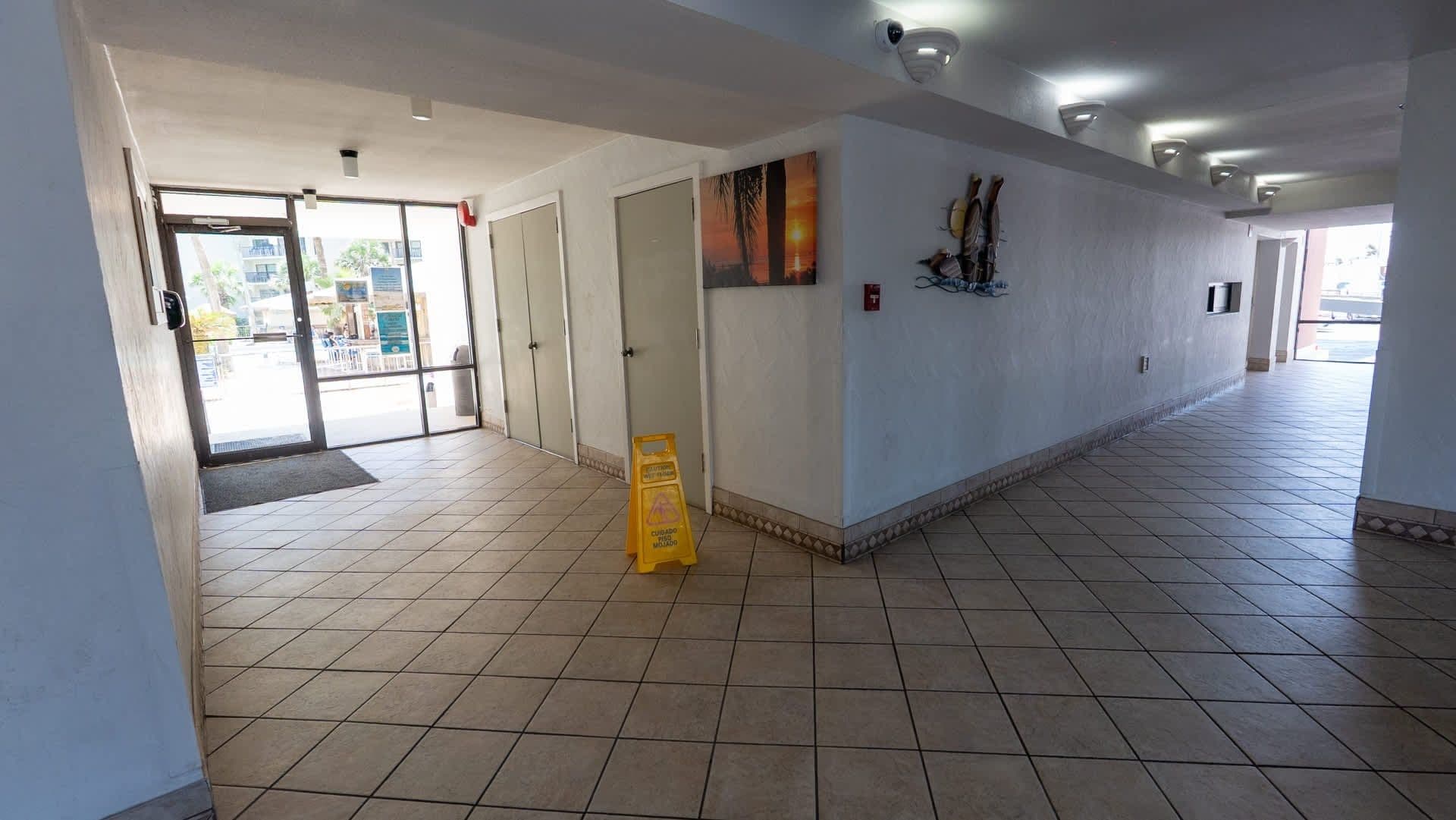 A spacious hallway with a tiled floor, a glass door entrance, and a yellow caution sign.