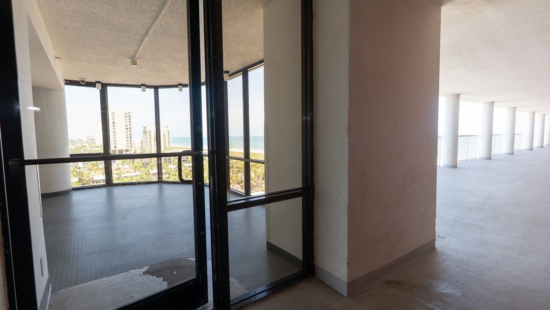 A spacious interior with large windows offering a view of a beach and high-rise buildings.