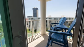 A balcony with a table and two chairs, overlooking a cityscape with modern buildings. - Saida Royale, Beachfront 10th Floor, 2br, 3 Pools 2 Bedroom Apts (South Padre Island)