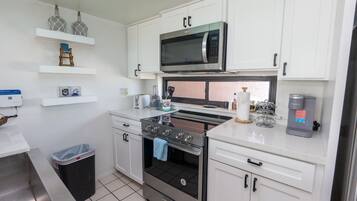 A compact kitchen with white cabinets, a stainless steel stove, a microwave, and a coffee machine.