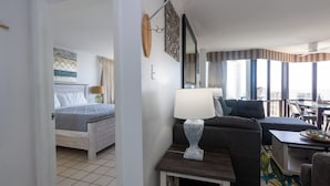 Ein Hotelzimmer mit einem Bett, einem Schlafsofa, einem Tisch mit Lampe und Blick auf die Stadt durch große Fenster.