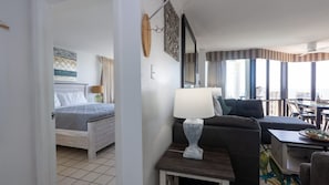 Habitación de hotel con cama, sofá, mesa con lámpara y vistas a la ciudad a través de amplios ventanales.
