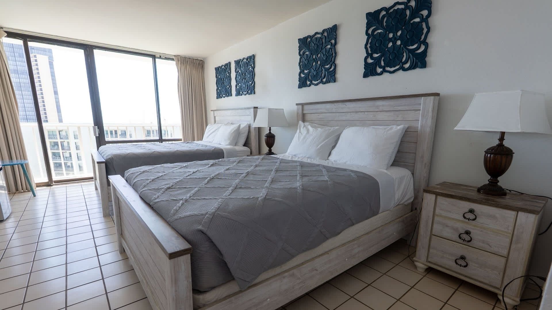 A hotel room with a large bed, two bedside tables, a window with curtains, and decorative wall art.