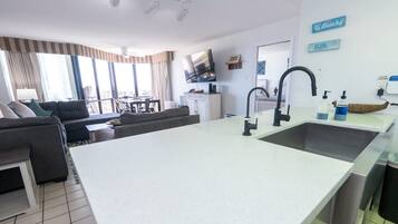 Una cucina moderna con una grande isola, un'area pranzo con divano e tavolo, e un soggiorno con divano e televisione.