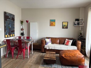 Ein Wohnzimmer mit einem braunen Ledersofa, roten Sesseln, einem Holztisch und einem Essbereich mit Tisch und Stühlen.