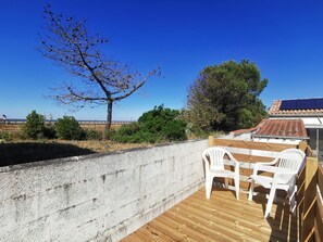 Eine Holzterrasse mit einer Betonmauer, einem Tisch mit Stühlen und Blick aufs Meer.