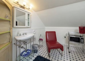 Une salle de bain avec un lavabo blanc, un miroir, une chaise rouge et un four à micro-ondes.