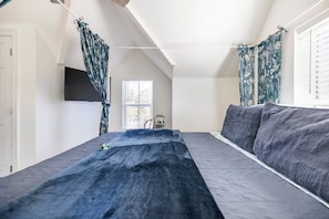 A bedroom with a bed, a TV mounted on the wall, and a window with curtains. - Las Ventanas | Romantic Two-Story Retreat (Pensacola)