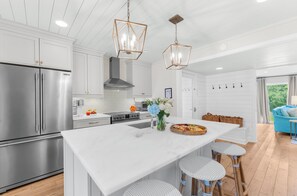 A modern kitchen with stainless steel appliances, a central island, pendant lighting, and a view to the living area. - Sunny, charming home short walk to beach (Seabrook Island)