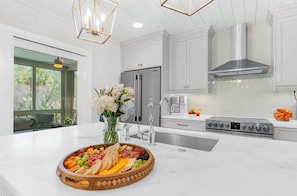 A modern kitchen with white cabinetry, stainless steel appliances, a central island with a fruit and cheese board, and a vase of flowers. - Sunny, charming home short walk to beach (Seabrook Island)