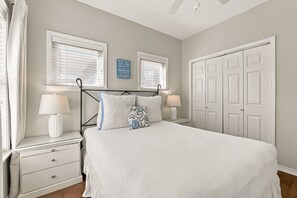 A bedroom with a bed, two bedside tables with lamps, a window with blinds, a door, and a wall-mounted sign. - 5BR Pet-Friendly Blue Mountain Beach Home | Gulf views & Community Pool (Santa Rosa Beach)