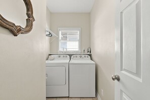 A laundry room with two white front-loading washing machines and a window with blinds. - 5BR Pet-Friendly Blue Mountain Beach Home | Gulf views & Community Pool (Santa Rosa Beach)