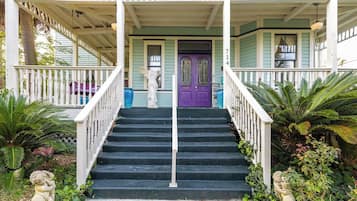 A porch with a staircase leading to a door, surrounded by plants and statues.