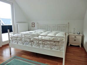 A white metal bed with a decorative headboard in a room with wooden flooring, a bedside table, and a nightstand. - Vacation home with a fireplace and infrared sauna, about 800 meters from the sandy beach, washing machine (Glowe)