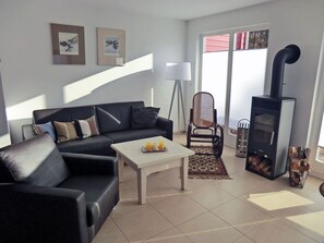 Un salon avec un canapé noir, une table basse blanche, un lampadaire, un tapis à motifs et un poêle à bois.