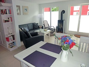 A modern living room with a sofa, a coffee table, a bookshelf, a fireplace, and a window with a view. - Vacation home with a fireplace and infrared sauna, about 800 meters from the sandy beach, washing machine (Glowe)