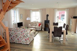 A living room with a sofa, a dining table, and a fireplace. - Vacation home with a fireplace and sauna, about 400 meters from the sandy beach; pets welcome (Glowe)