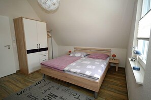 Ein Schlafzimmer mit Bett, Kleiderschrank, Nachttisch, Lampe und einem Fenster.