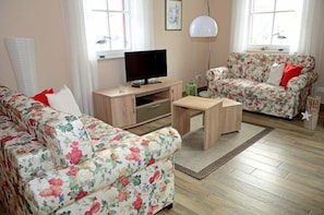 A living room with a sofa, a coffee table, a TV, and a floral-patterned couch. - Vacation home with a fireplace and sauna, about 400 meters from the sandy beach; pets welcome (Glowe)
