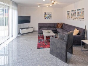 A modern living room with a grey sectional sofa, a coffee table, and a flat-screen TV mounted on the wall. - Holiday Home With 2 Bedrooms (Esens)