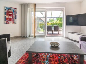 A modern living room with a dining table, a flat-screen TV, and a sliding glass door leading to an outdoor patio. - Holiday Home With 2 Bedrooms (Esens)