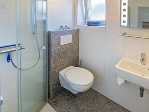 A bathroom with a glass shower enclosure, a white toilet, a sink with a mirror, and a window with a towel. - Holiday Home With 2 Bedrooms (Esens)
