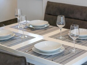 A dining table set with white plates and clear wine glasses, accompanied by a brown upholstered sofa. - Holiday Home With 2 Bedrooms (Esens)