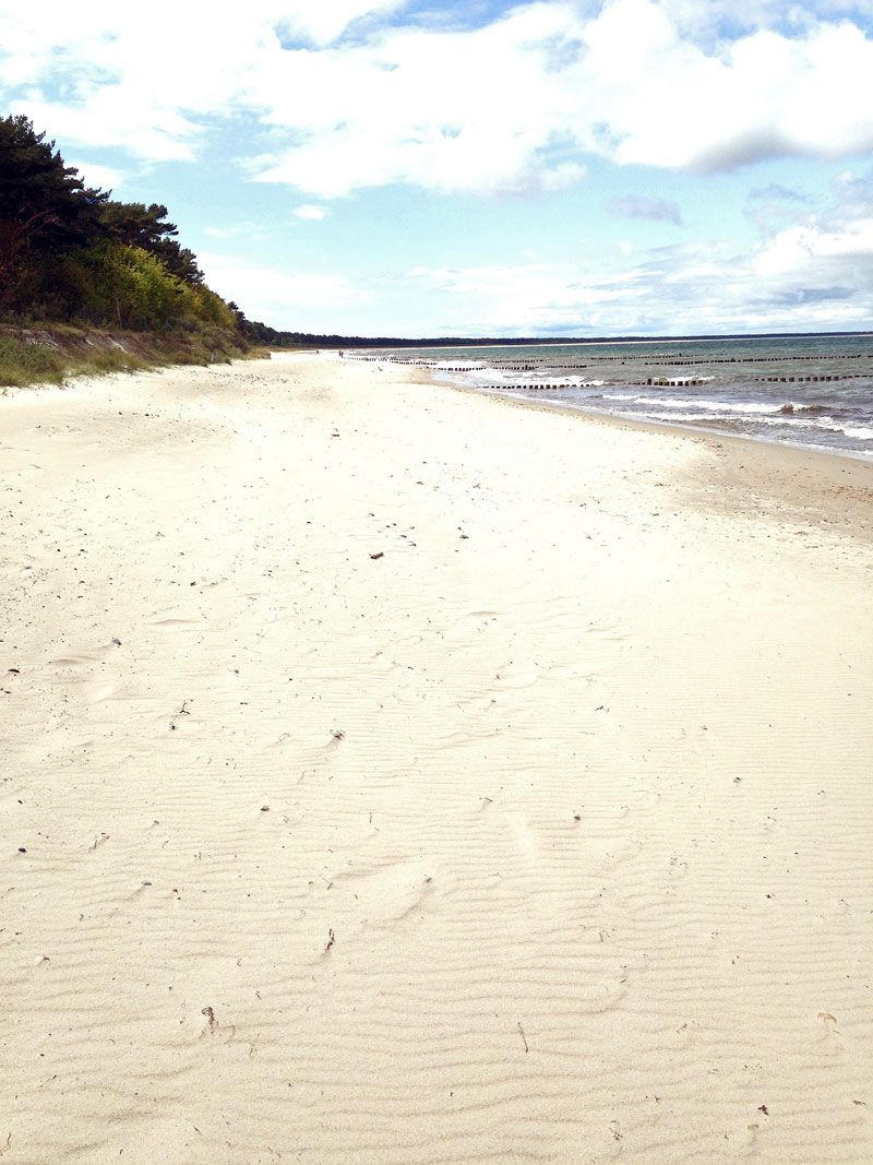 Ein Sandstrand mit einer hölzernen Promenade, die zum Wasser führt.