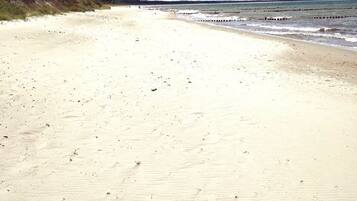 Ein Sandstrand mit einer hölzernen Promenade, die zum Wasser führt.