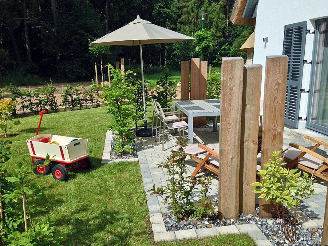 A patio area with a table and chairs, surrounded by a wooden fence, and a small garden with plants and a wheelbarrow.