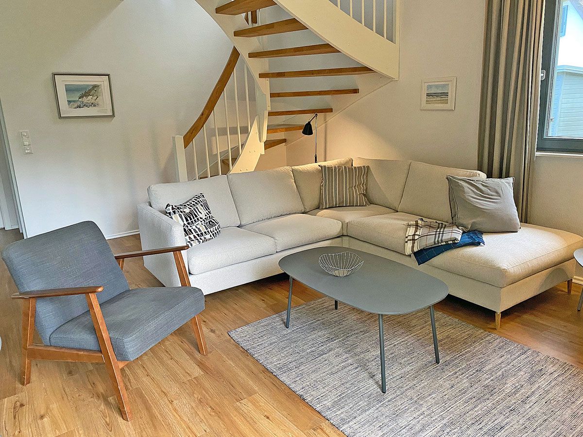 A living room with a wooden staircase, a grey armchair, a sofa set, and a coffee table.