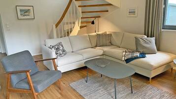 A living room with a wooden staircase, a grey armchair, a sofa set, and a coffee table.