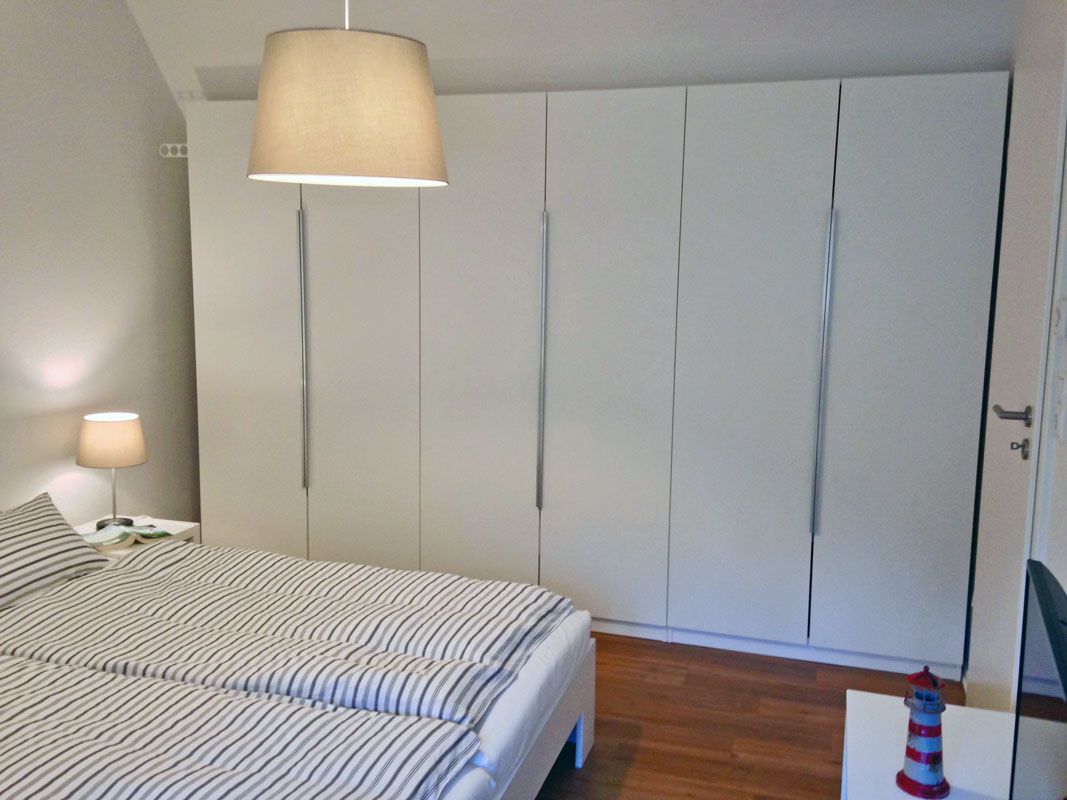 A bedroom with a bed, a wardrobe, a nightstand, a lamp, and a small decorative item.