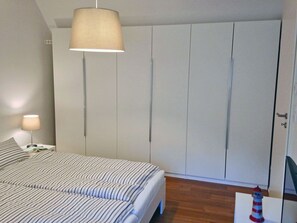 Ein Schlafzimmer mit Bett, Schrank, Nachttisch, Lampe und einem kleinen dekorativen Gegenstand.