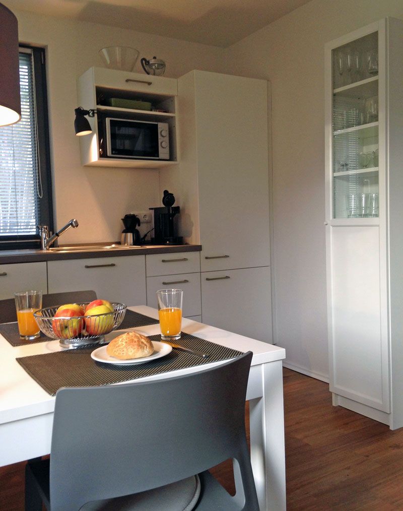 Eine Küche mit Mikrowelle, Spüle und einem Schrank mit Glastüren. Ein Tisch ist gedeckt mit Essen und Gläsern Orangensaft.