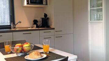 Eine Küche mit Mikrowelle, Spüle und einem Schrank mit Glastüren. Ein Tisch ist gedeckt mit Essen und Gläsern Orangensaft.