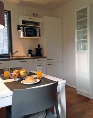 Eine Küche mit Mikrowelle, Spüle und einem Schrank mit Glastüren. Ein Tisch ist gedeckt mit Essen und Gläsern Orangensaft.