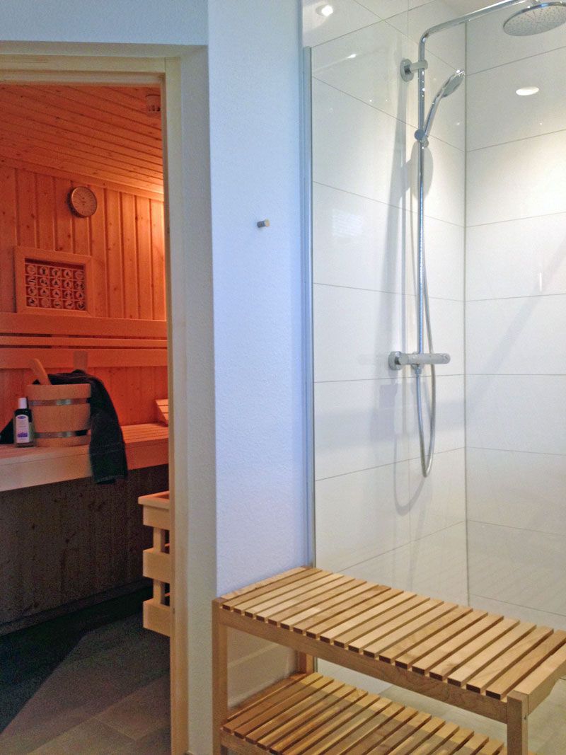 A shower area with a glass door, a wooden bench, and a towel rack.