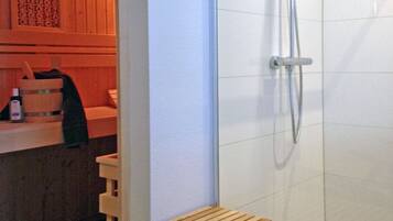 A shower area with a glass door, a wooden bench, and a towel rack.